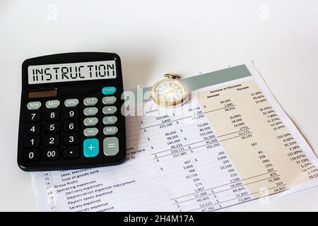 On the display of the calculator the word INSTRUCTION. On a white background financial document and clock Stock Photo