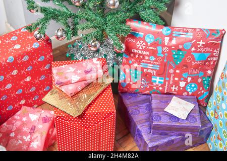 Christmas presents. packages wrapped with colored paper on the ground under the Christmas tree decorated with balls and red ribbon Stock Photo