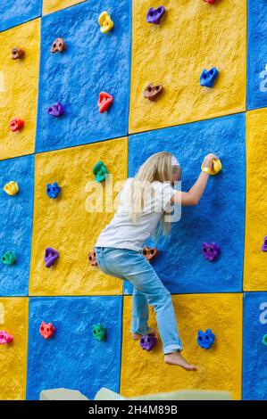 A little Girl Climbs a Stone Wall in a children's center. Stock Photo