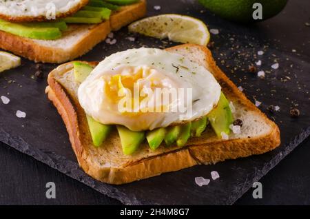 Avocado sandwich with scrambled eggs on dark background. Bread with fresh sliced avocados top view. Stock Photo