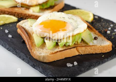 Avocado sandwich with fried egg - sliced avocado and egg on toasted bread for healthy breakfast or snack. Stock Photo