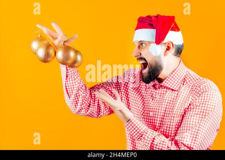 a man in a Christmas Santa hat holds Christmas toys, balls and shouts in his hand. Stock Photo