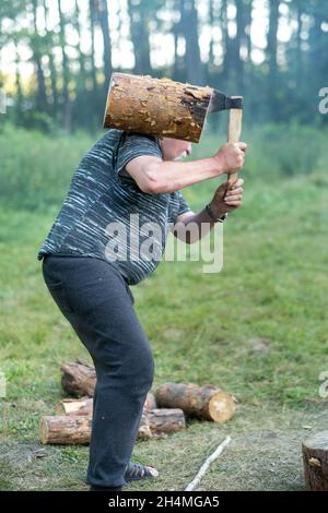 a man in the forest chopping wood with a steel axe, a forest landscape with a woodcutter. Stock Photo