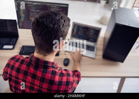 Back rear spine view photo of young man sit desk work code develop software write indoors inside office workplace Stock Photo