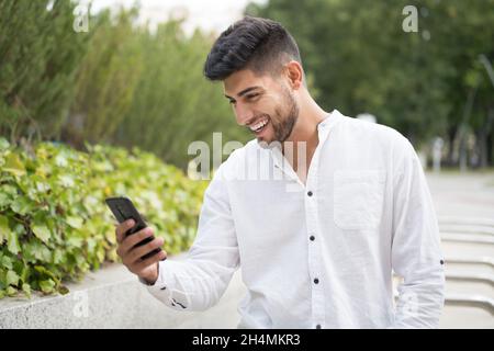Handsome mixed race young man, smiling, using a mobile phone outdoors. High quality photo Stock Photo