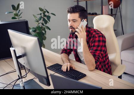 Photo of serious focused young man write computer programmer hold phone talk indoors inside office workplace Stock Photo