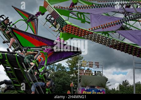 A fully loaded kite ride with smiling children in the foreground against a dramatic cloudy sky at the Deerfield Fair - Deerfield, New Hampshire Stock Photo