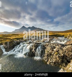 A waterfall on Allt Dearg Mor river with the Black Cuillin mountains in the distance with cloud bank above, Sligachan, Isle of Skye, Scotland, UK Stock Photo