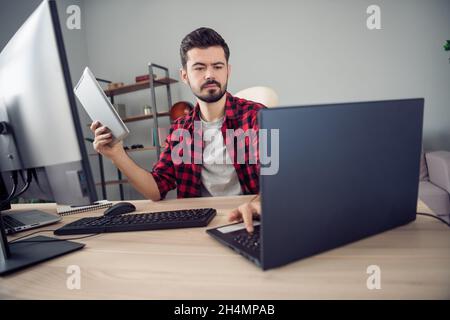 Photo of serious concentrated young man look laptop write hold tablet sit desk inside office indoors Stock Photo