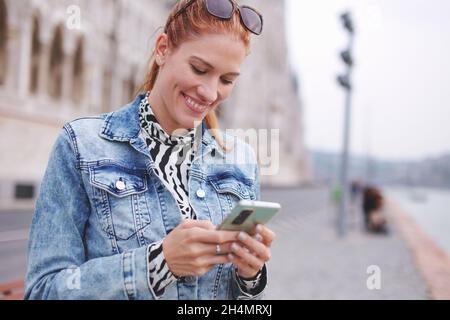 Happy young Caucasian redhead woman messaging on smartphone Stock Photo