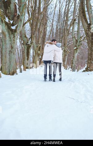 Young happy couple smile to each other and walk in winter park holding hands. Man and woman have fun together during winter holidays Stock Photo