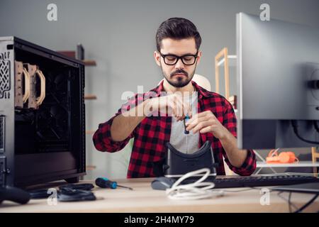 Portrait of attractive focused experienced skilled guy fixing vr cyberspace helmet at studio office work place station indoor Stock Photo