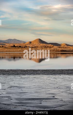 A hill is reflected in a partially frozen lake, Boulder Reservoir, with ice in the foreground Stock Photo