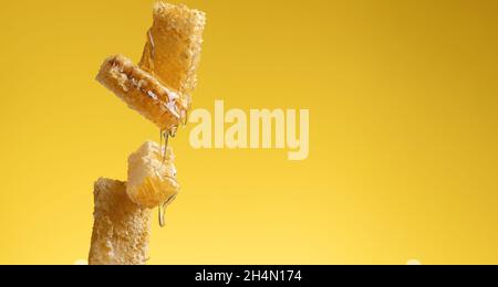 flowing honey over honeycomb on yellow background, banner. Copy space Stock Photo