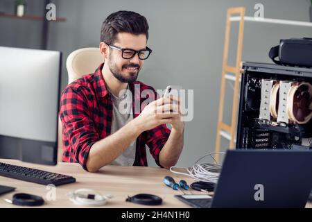 Portrait of attractive focused trendy cheerful guy engineer using device gadget browsing web bug report at office workplace workstation indoor Stock Photo