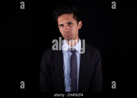 Latin business man with sad face, isolated on black background. Young adult frustrated young man doing bad business. Stock Photo