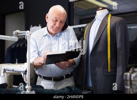 Professional tailor man talking on mobile phone and making notes in notebook Stock Photo