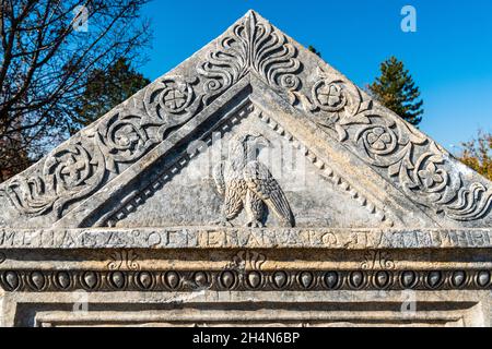 Cavdarhisar, Kutahya, Turkey – November 17, 2020. Triangular pediment of a marble grave stele depicting an eagle with head turned backwards, curved br Stock Photo