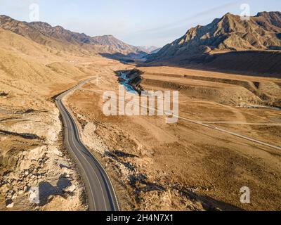 winding mountain road leading up. Top view of mountain road and the river surrounded by high mountains on the brown earth Stock Photo