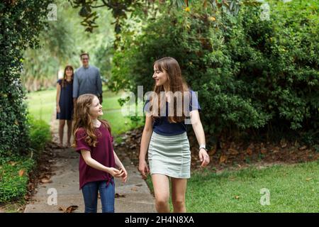 A family of a mother and father and two daughters taking a walk in the neighborhood on the sidewalk outside in the summer Stock Photo