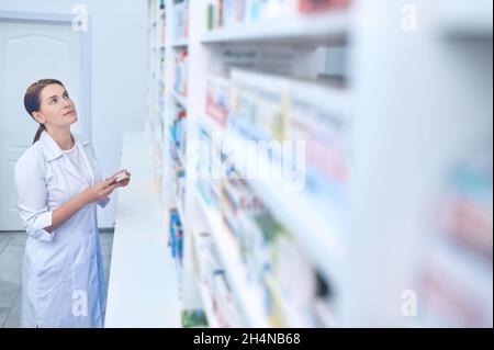 Woman in medical gown choosing medicine at pharmacy Stock Photo