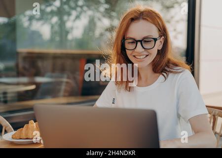 Beautiful redhead professional woman freelancer works on laptop computer poses in outdoor cafe Stock Photo