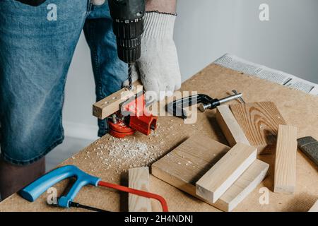 Close-up of the hands of a professional worker holding electrical equipment and drilling holes in a wooden board. The concept of home renovation. DIY. Stock Photo
