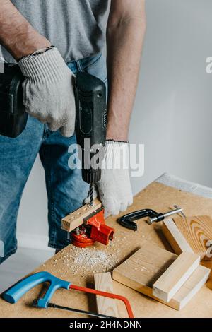 Close-up of the hands of a professional worker holding electrical equipment and drilling holes in a wooden board. The concept of home renovation. DIY. Stock Photo