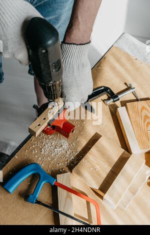 Close-up of the hands of a professional worker holding electrical equipment and drilling holes in a wooden board. The concept of home renovation. DIY. Stock Photo