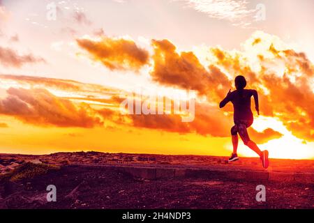 Fitness training sports athlete running in sunset - Silhouette of girl jogging on trail road with orange sky background. Fit woman exercise lifestyle Stock Photo