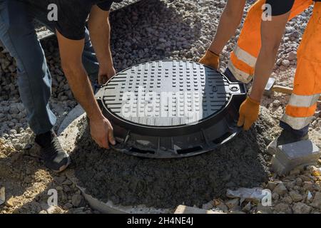 A worker installs a sewer manhole on a septic tank made of concrete rings Stock Photo