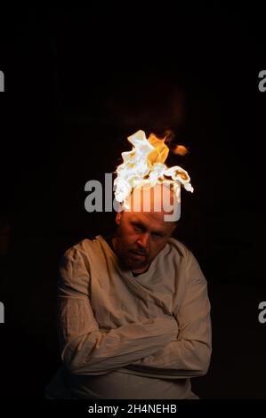 Bald man in a straitjacket with a burning head on a dark background. Stock Photo