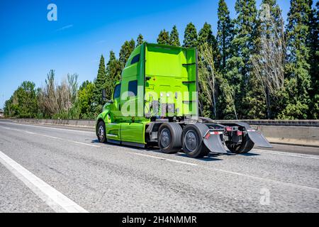 Industrial grade professional use bright green powerful big rig semi truck tractor without the semi trailer running on the wide highway road to wareho Stock Photo