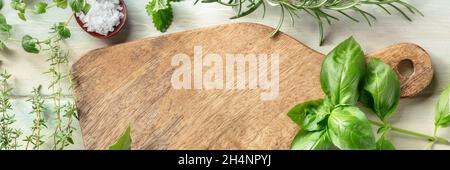 Cooking with herbs panorama. A wooden cutting board with salt and aromatic herbs. Basil, rosemary, and thyme, top shot. Culinary design template Stock Photo