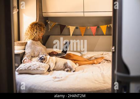 Attractive woman have relax inside van camper laying on bed and using laptop computer connection. Adorable dog sleeping near her. Female independent p Stock Photo