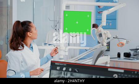 Woman analyzing green screen on monitor and teeth x ray for dental examination. Dentist using chroma key and mockup display for checkup while looking at radiography for oral care Stock Photo