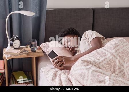 African young woman lying on the bed and using her mobile phone before sleeping Stock Photo