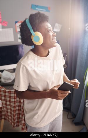 African happy woman enjoying her dancing while listening to music in wireless headphones at home Stock Photo