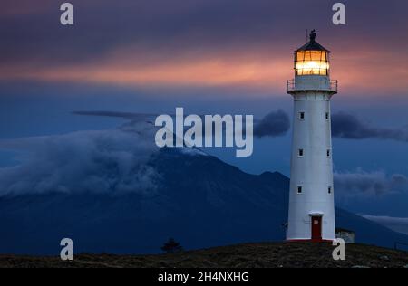 Cape Egmont Lighthouse and Taranaki Mount on background, New Zealand Stock Photo