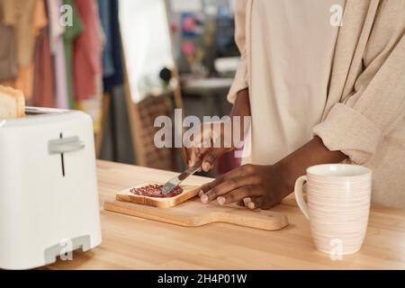 Close-up of African woman applying jam on bread while cooking at the kitchen table at home Stock Photo