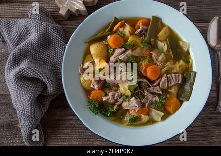 Plate with delicious vegetable soup with pork meat for autumn and winter season. Cooked with cabbage, potatoes, carrots, pumpkin, green beans and herb Stock Photo