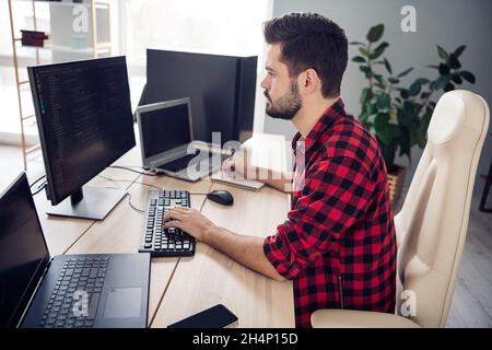 Profile side photo of serious young man look screen write code web design sit desk indoors inside office workplace Stock Photo