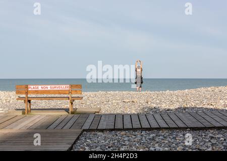 Lady alone facing the sea, making arm movements, on a pebble beach in Cayeux-sur-Mer. Opal Coast, France Stock Photo