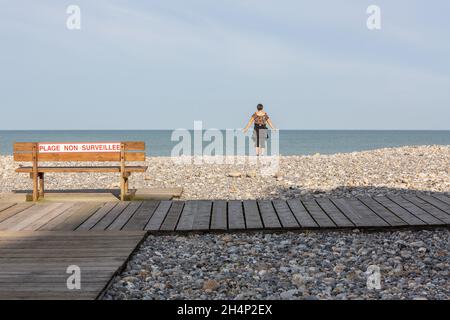 Lady alone facing the sea, making arm movements, on a pebble beach in Cayeux-sur-Mer. Opal Coast, France Stock Photo