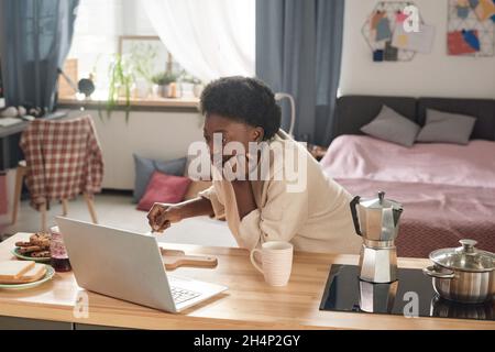 African woman watching something on laptop at the table during her breakfast in the morning Stock Photo