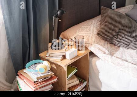 Close-up of bed table with alarm clock, glass of water and books on it near the bed Stock Photo