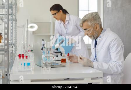 Senior male scientist doing experiments in laboratory by pipetting samples of cell culture medium. Stock Photo