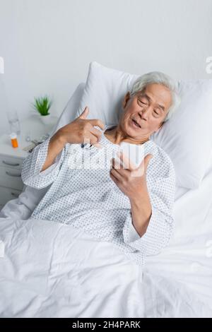 Senior asian patent with pulse oximeter using smartphone on bed in clinic Stock Photo