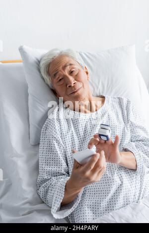 Elderly asian patient with pulse oximeter using smartphone in hospital ward Stock Photo