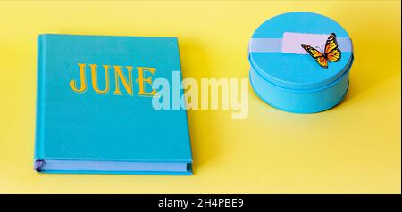 Text June on a turquoise notebook and yellow background, next to a turquoise box and butterfly Stock Photo